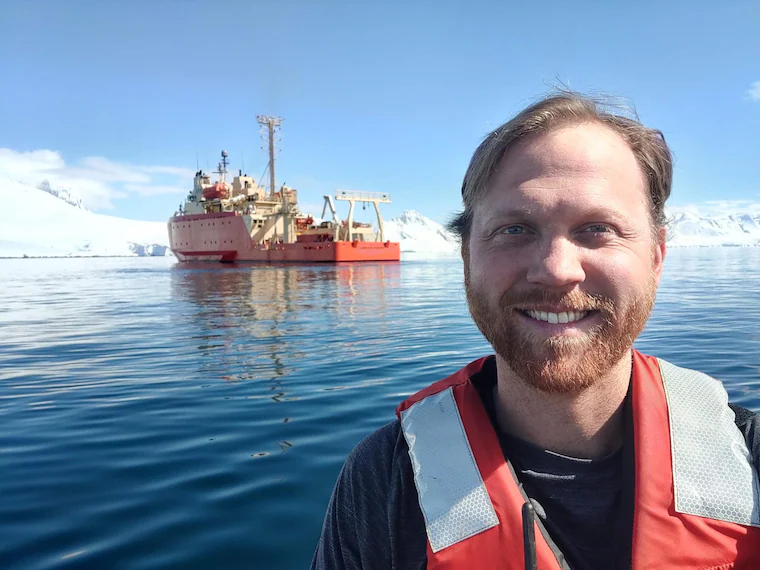 Stewart on the water in Antarctica with the research vessel Laurence M. Gould behind him
